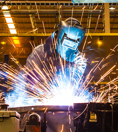 front view of welder technician working on metal, sparks flying off 